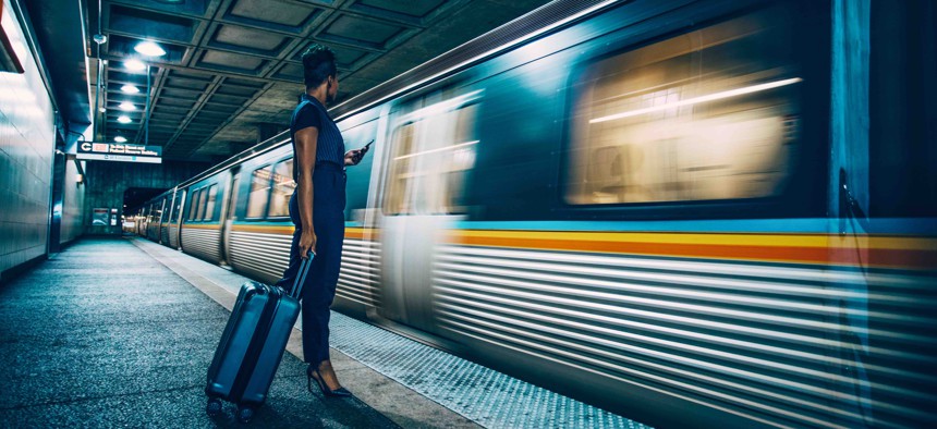 A businesswoman waits on a platform as a subway train approaches.