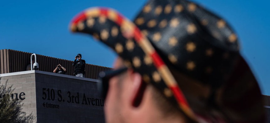 Members of law enforcement stand watch over a gathering on a sidewalk in protest of the election process in front of the Maricopa County Tabulation and Election Center on November 14, 2022 in Phoenix, Arizona.